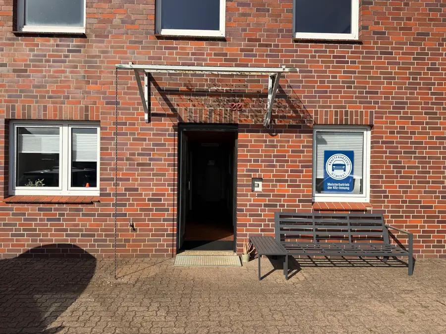 Hauseingang des Autohauses mit Sitzbank und dem Schild der Kfz-Innung